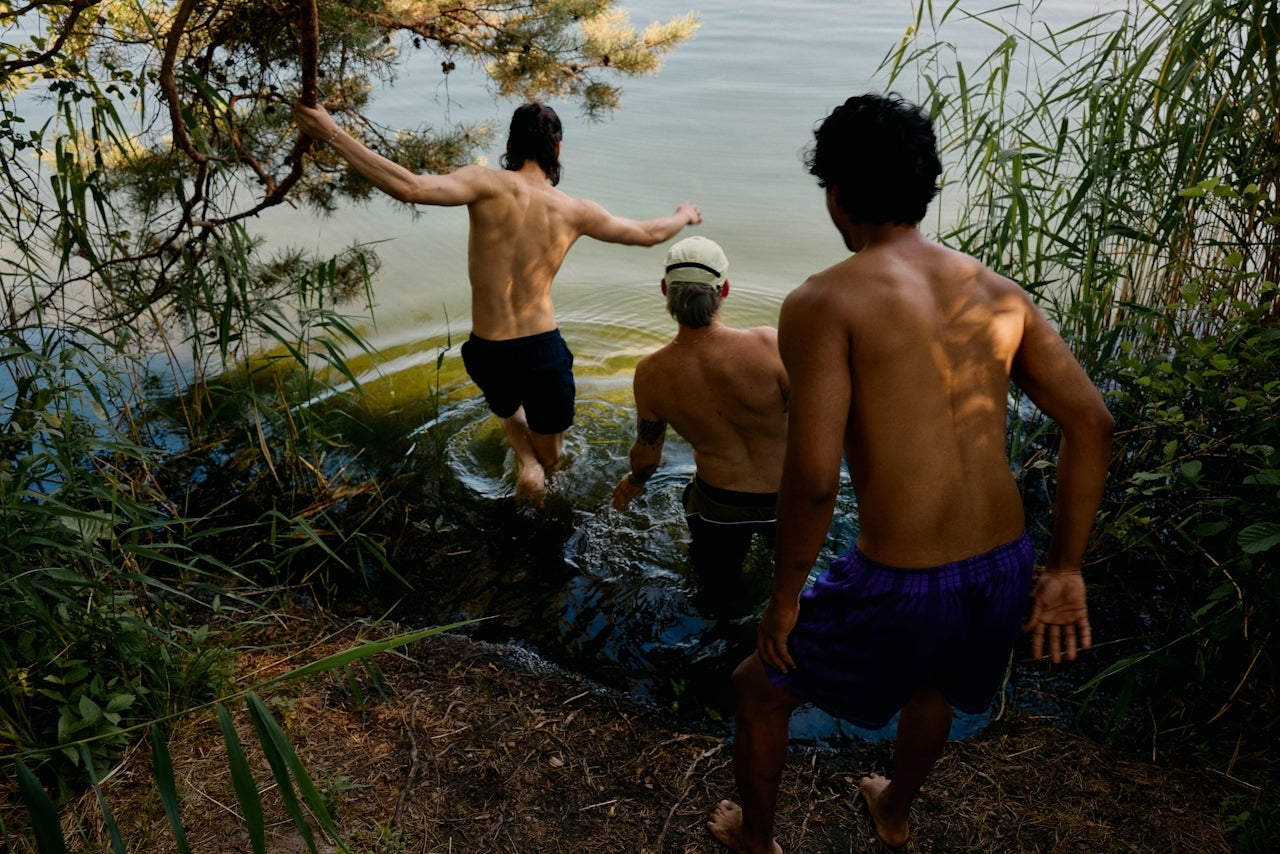 Three men standing by a body of water with trees and foliage around.