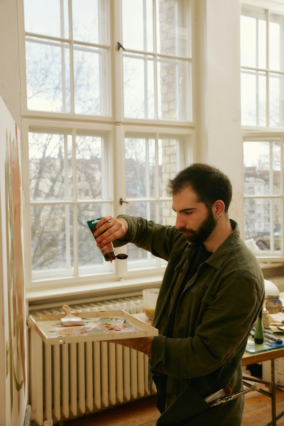 Man holding paint in a room with large windows and a radiator.