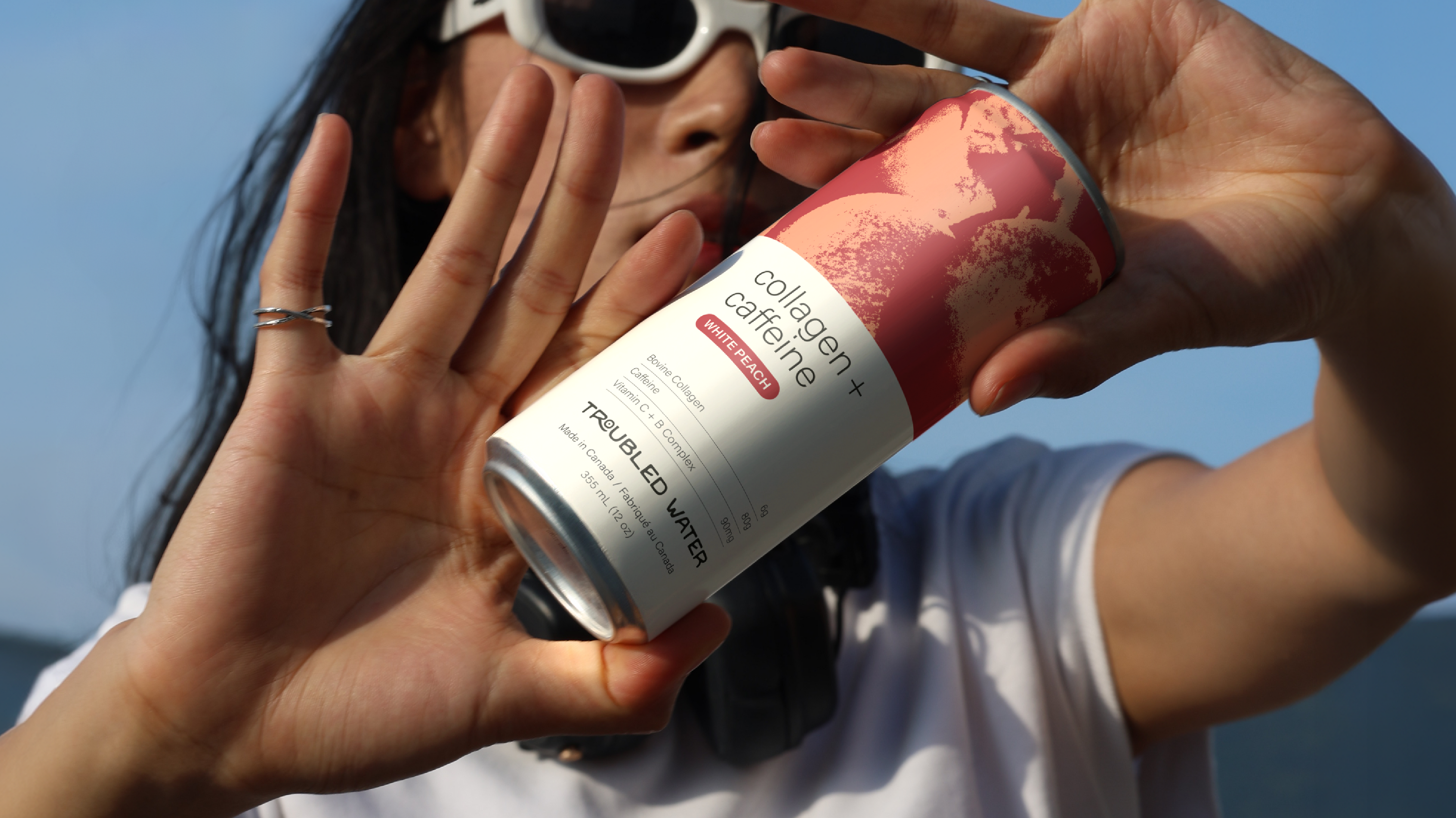 Person holding a can of Troubled Water against a clear blue sky