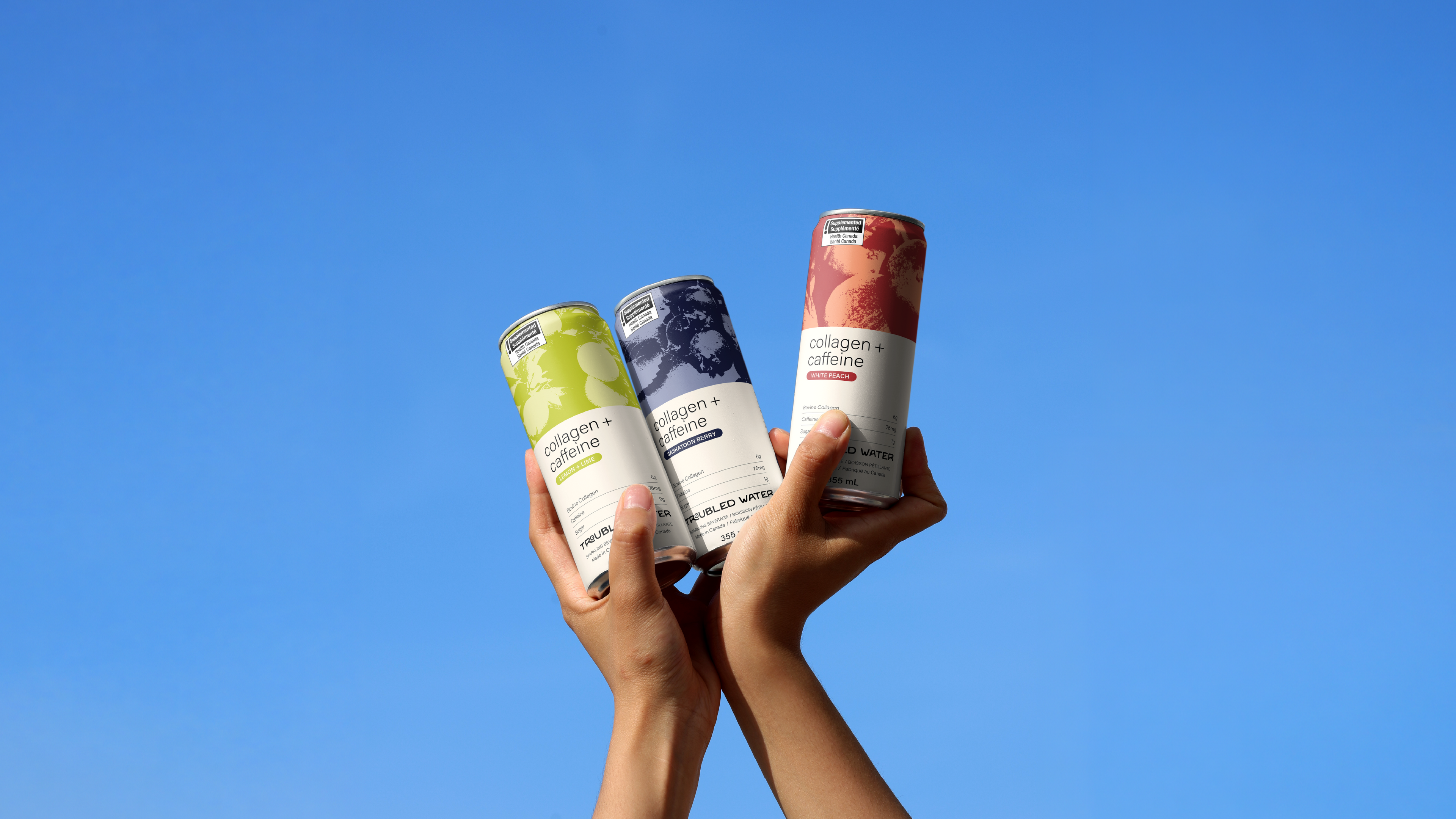 Two hands holding all three flavours of Troubled Water cans
