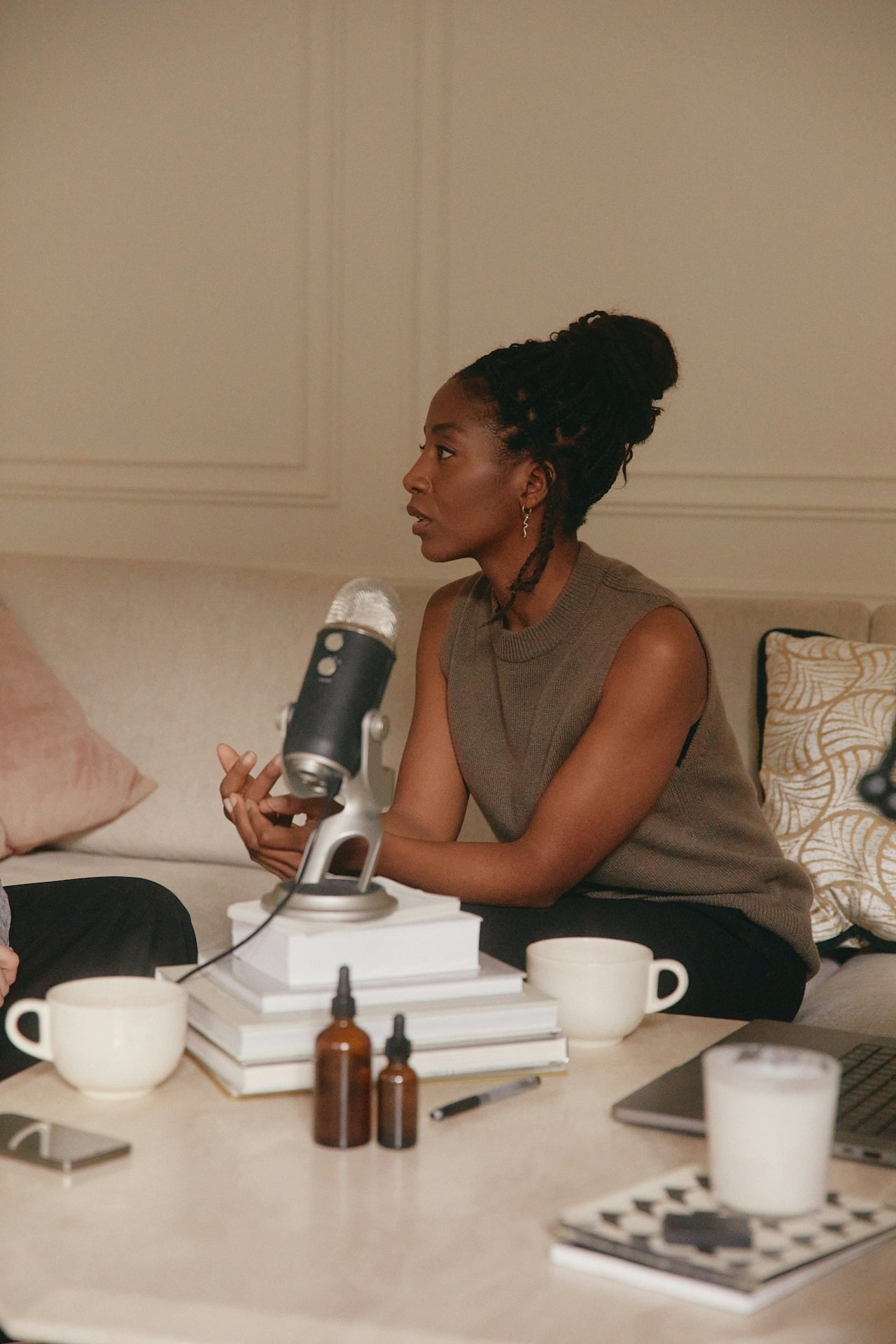 Woman sitting on a couch with a microphone, books, and coffee cups on a table.