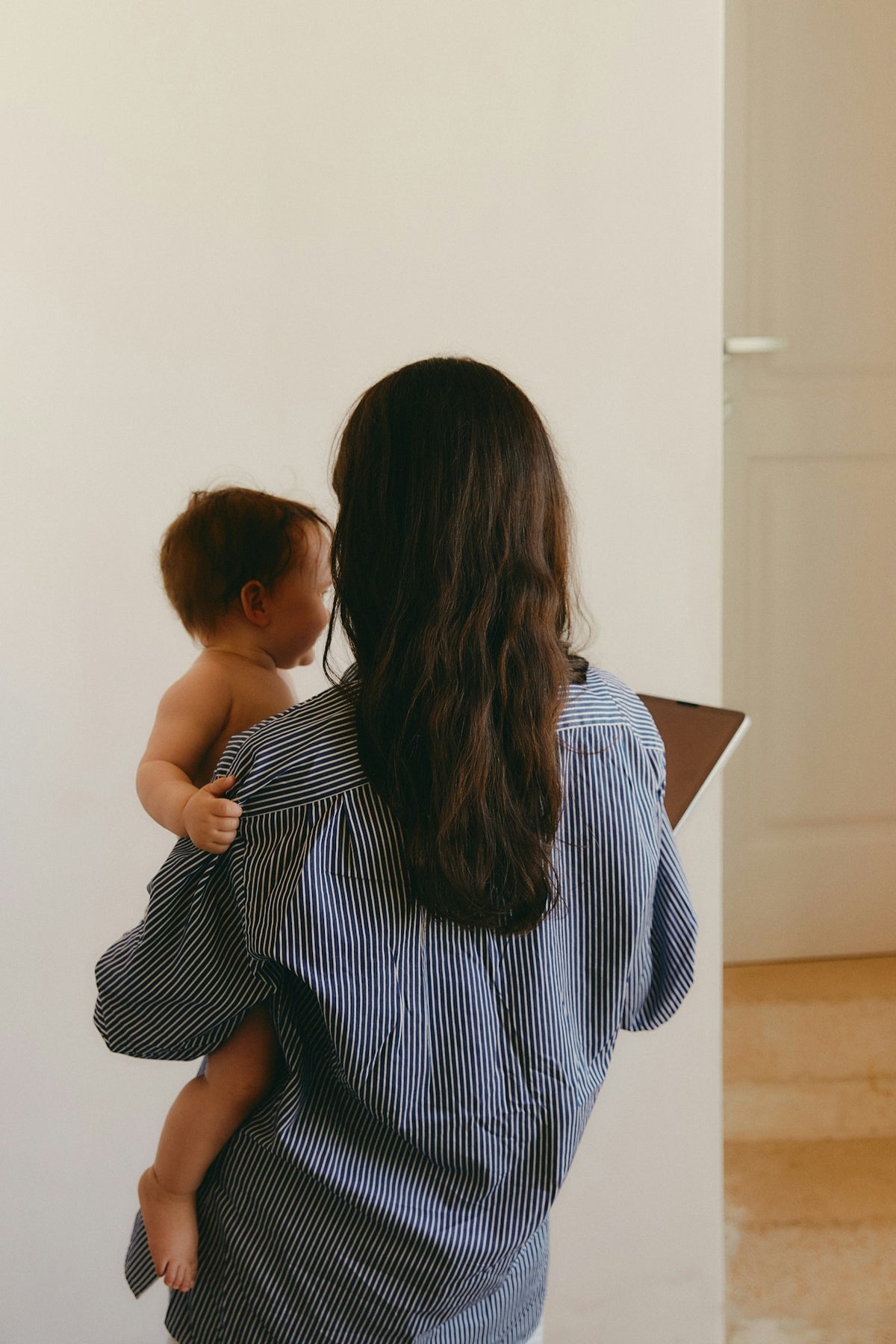 Woman holding a baby in a room with a white wall and wooden floor.
