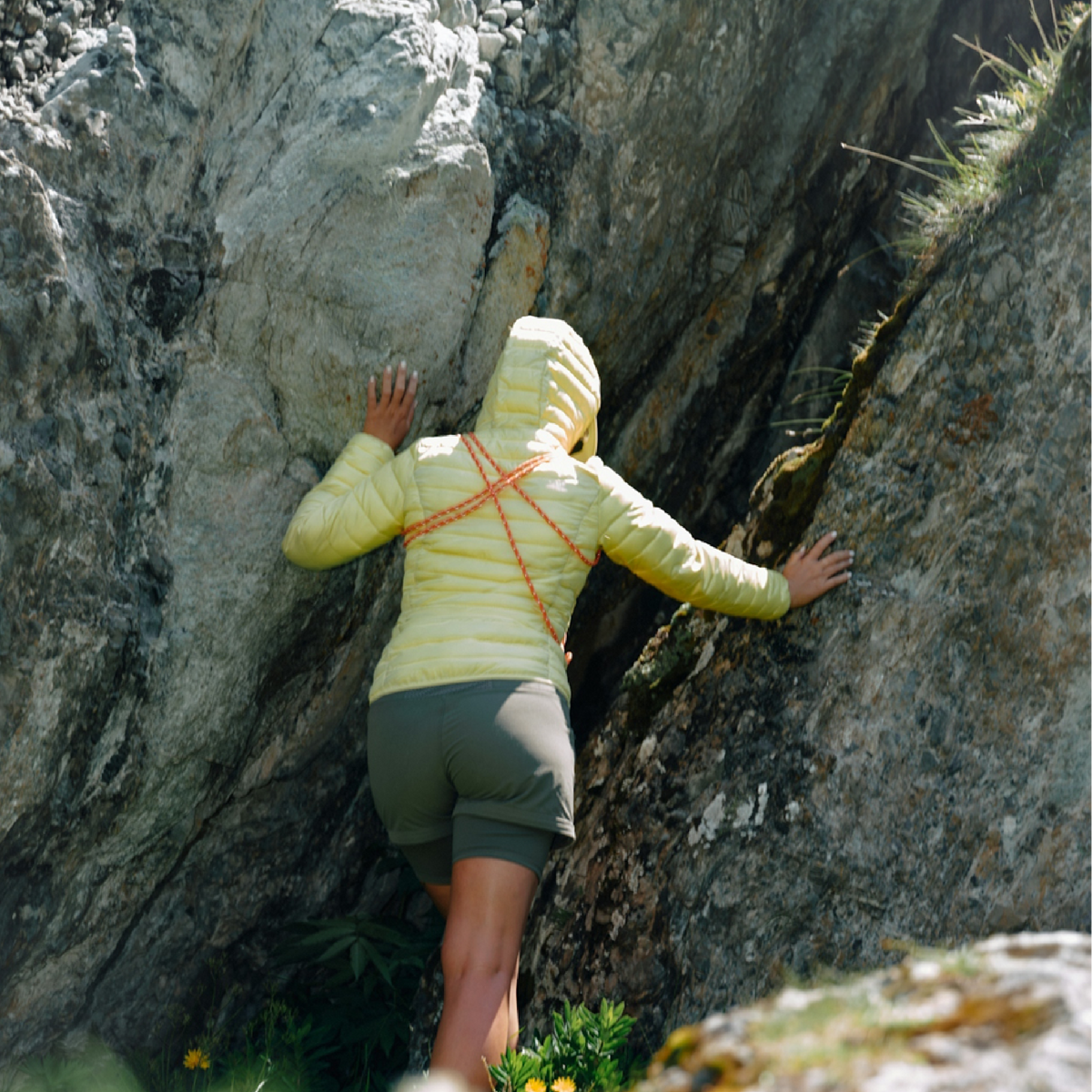 Person climbing a rocky mountain face wearing a yellow jacket.
