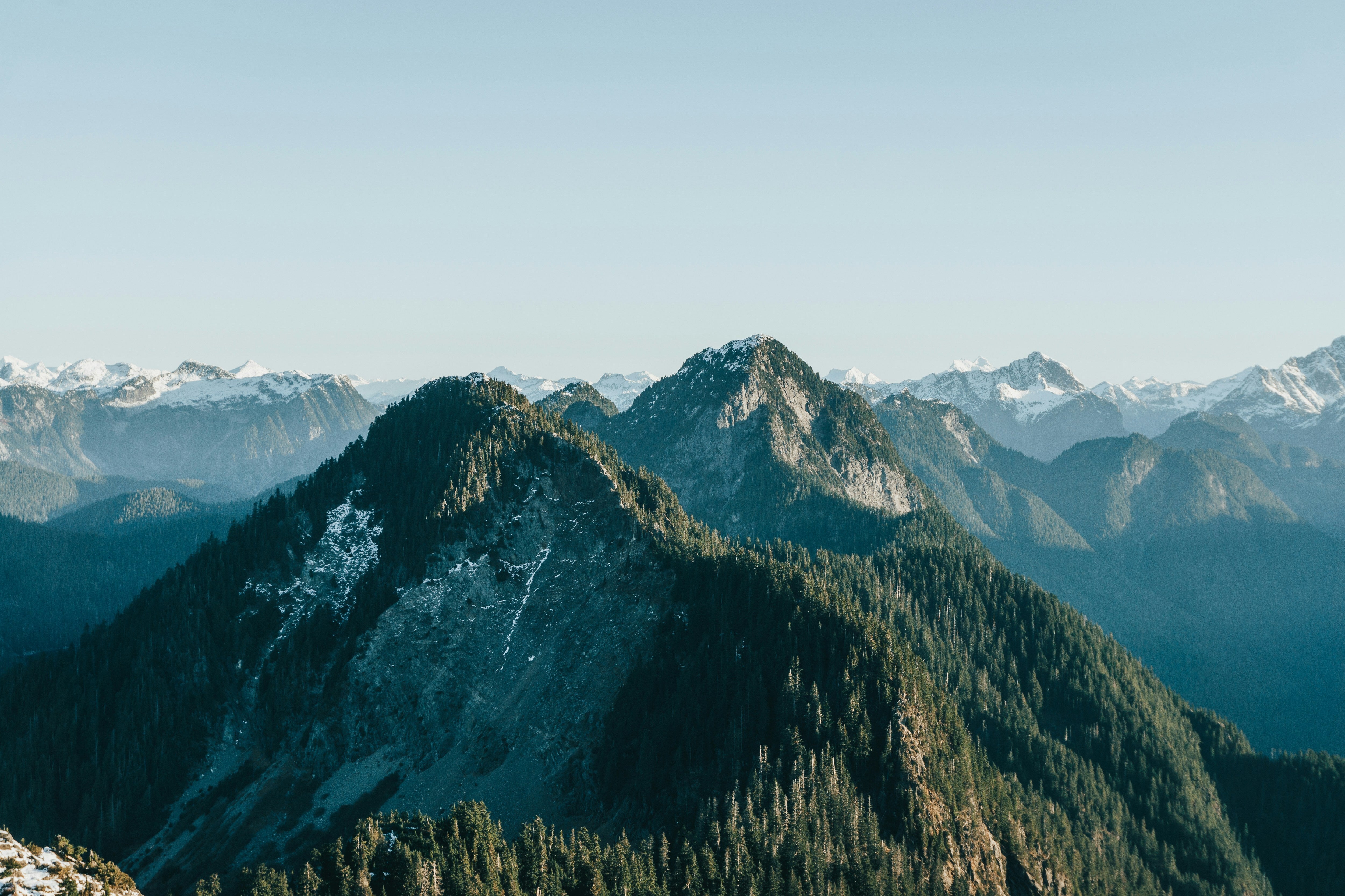 Mountain range with snow-capped peaks and forested slopes under a clear sky.